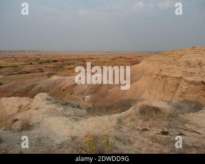 Vue panoramique sur les mounds dorés du parc national des Badlands, dans le Dakota du Sud, avec fleurs sauvages jaunes au premier plan. Banque D'Images