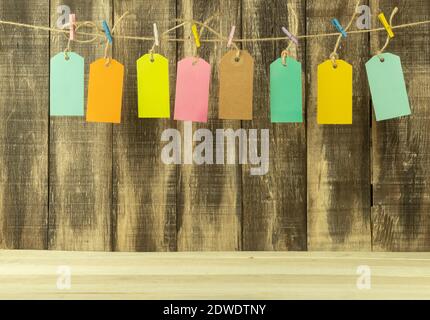 Huit étiquettes de prix de différentes couleurs avec espace pour le texte. Balises et inscriptions pour le texte sur fond en bois. Les étiquettes sont accrochées sur une corde avec mu Banque D'Images