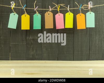 Huit étiquettes de prix de différentes couleurs avec espace pour le texte. Balises et inscriptions pour le texte sur fond en bois. Les étiquettes sont accrochées sur une corde avec mu Banque D'Images