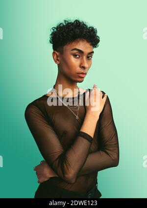 Homme androgyne en t-shirt en maille noire. Homme transgenre posant sur fond bleu. Banque D'Images