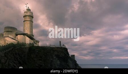 Phare spectaculaire sur un rocher avec un ciel nuageux et spectaculaire en arrière-plan. Situé dans 'Cantabria' Espagne idéal pour les papiers peints. Banque D'Images