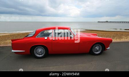 Voiture automobile classique Red Peerless GT stationnée sur la promenade du front de mer avec la plage et la mer en arrière-plan. Banque D'Images