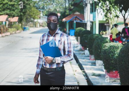 Portrait d'un professeur africain gai dans un masque debout à l'extérieur école Banque D'Images