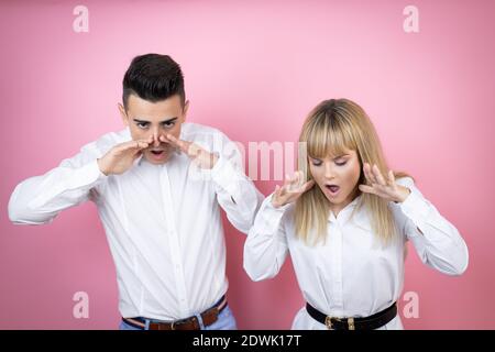 Jeune couple de petite amie et petit ami sur fond rose isolé crier et crier à voix haute avec les mains sur la bouche Banque D'Images