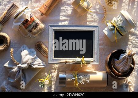 Tableau noir avec espace de texte. Plat avec des cadeaux de Noël sans gaspillage. Cadeau de Noël emballé dans une serviette, des tasses en bambou, des bols, un ballon isolé. Durable Banque D'Images