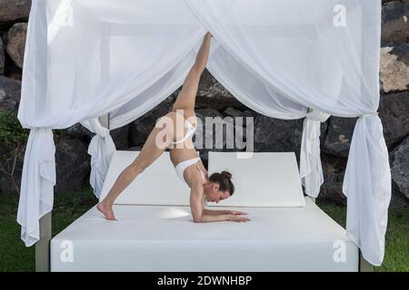 Vue latérale d'une femme flexible portant le maillot debout vers le bas Face à l'asana du chien sur le lit à baldaquin et pratiquer le yoga Banque D'Images