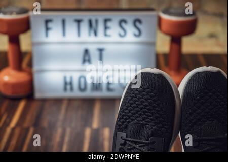 Concept de fitness à la maison. Gros plan sur les chaussures de course à pied avec un panneau de visionneuse flou et un texte FITNESS À LA MAISON en arrière-plan. Faire de l'activité à la maison. Coronavi Banque D'Images