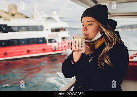 La main d'une femme tient une tasse blanche de chaud boisson lactée à la cannelle appelée sahlep de salep turc sur le Fond de l'eau ondulée et de la brumeuse Ma Banque D'Images