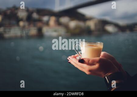 La main d'une femme tient une tasse blanche de chaud boisson lactée à la cannelle appelée sahlep de salep turc sur le Fond de l'eau ondulée et de la brumeuse Ma Banque D'Images