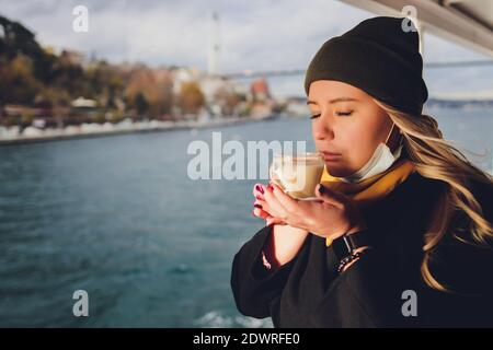 La main d'une femme tient une tasse blanche de chaud boisson lactée à la cannelle appelée sahlep de salep turc sur le Fond de l'eau ondulée et de la brumeuse Ma Banque D'Images