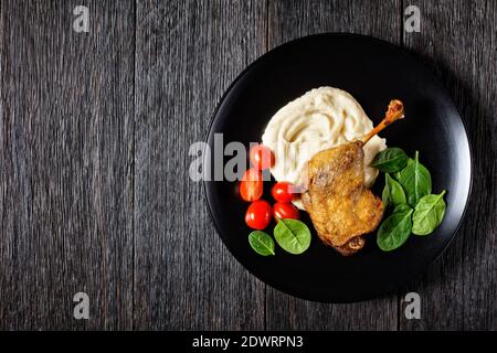 Cuisine française - cuisse de canard rôtie - confit de canard avec purée de panais et sauce à l'orange, avec feuilles d'épinards fraîches servies sur une assiette blanche sur un bois sombre Banque D'Images