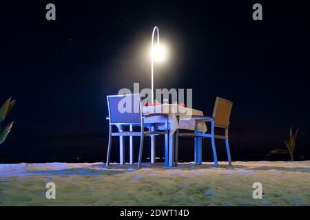 Table à manger sur la plage de sable la nuit, dîner romantique dans un complexe de luxe, Maldives. Banque D'Images