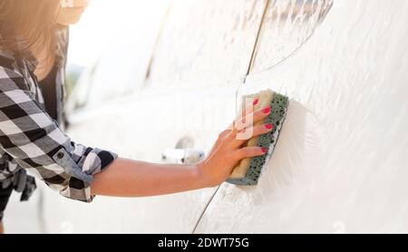 Main de fille avec éponge de nettoyage de voiture en utilisant la mousse sur la voiture laver Banque D'Images