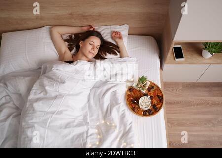 Femme dormant sur le lit avec un cadeau et un café avec des guimauves debout près d'elle. Surprise mornig Banque D'Images