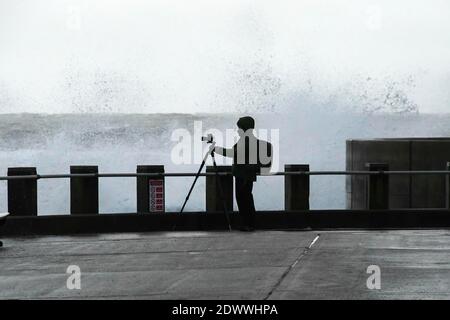 West Bay, Dorset, Royaume-Uni. 23 décembre 2020. Météo Royaume-Uni. Un photographe qui prend des photos des mers orageux alors qu'elles s'écrasont contre les défenses de la mer à West Bay à Dorset lors d'un après-midi de pluie et de vents violents. Crédit photo : Graham Hunt/Alamy Live News Banque D'Images