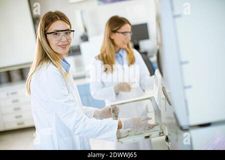 Jeunes femmes scientifiques dans un flacon de mise en blouse de laboratoire blanc avec un échantillon pour une analyse sur un système d'ionchromatographie en laboratoire biomédical Banque D'Images