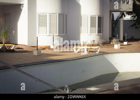 Complexe d'appartements abandonné avec piscine vide et chaises longues. Crise pandémique Covid-19, destinations touristiques concepts de verrouillage Banque D'Images