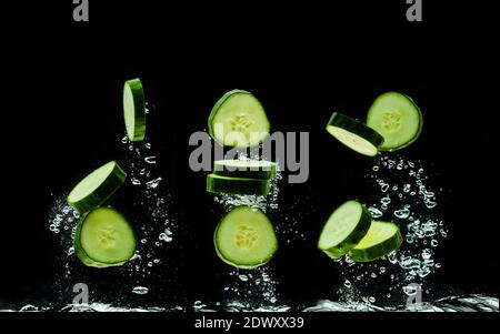 Tranches de bio concombre éclaboussant de l'eau isolée sur fond noir. Banque D'Images