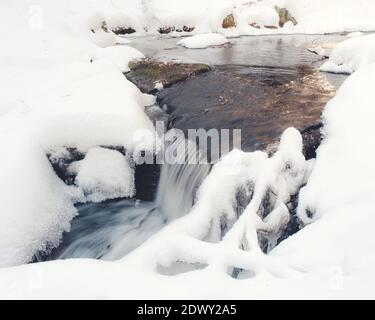 Une section de cascades sur une rivière glaciale après une chute de neige au début de l'hiver. Les ombres ont un ton bleu et la met en évidence un ton orange. Banque D'Images