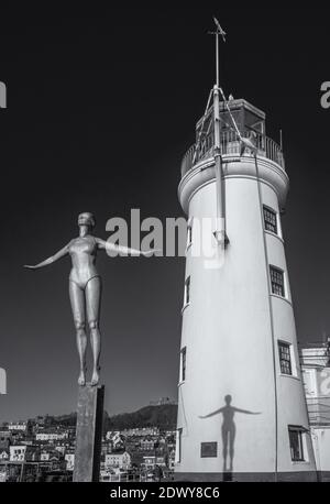 Le phare de Scarborough avec une figure commémorative avec des bras étirés devant. L'ombre de la statue tombe sur le phare blanc. Banque D'Images