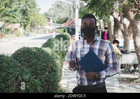 Portrait d'un professeur africain dans un masque de visage debout à l'extérieur école Banque D'Images