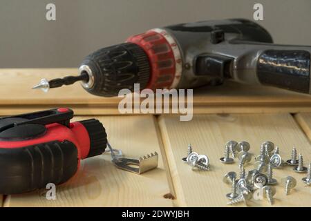 Perceuse et vis sans fil. Perceuse électrique avec forets, vis sur fond en bois. Bouquet de vis sur planches en bois. Outils assortis. Le beau profane Banque D'Images