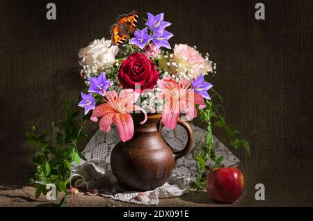 Encore la vie avec un bouquet de différentes fleurs dans une carafe et une pomme sur un fond de burlap. Mise au point sélective Banque D'Images