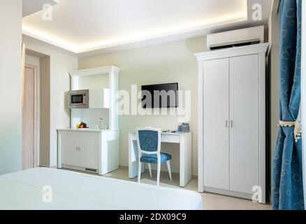 Intérieur de style classique blanc et bleu de la chambre d'hôtel avec module de cuisine armoire de placard, armoire et table de TV dans un espace simple de petit studio moderne Banque D'Images