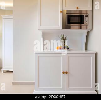 Vue avant de l'armoire modulaire de la mini-cuisine avec micro-ondes et assiette de fruits. Intérieur de style classique de la pièce blanche avec mur vide de l'espace de copie Banque D'Images