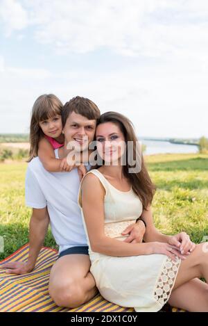 Jeune homme de famille femme et enfant fille, en été dans le parc, s'asseoir sur une couverture, se détendre parler, détente en plein air posant. Concept d'une famille heureuse Banque D'Images