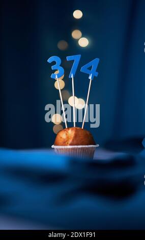 Gâteau d'anniversaire ou muffin avec le numéro trois cent soixante-quatorze (374) et des lumières sur fond bleu. Concept anniversaire ou anniversaire Banque D'Images