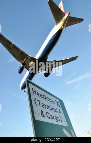 Avion de ligne British Airways qui atterrit à l'aéroport de Londres Heathrow à Hounslow, Londres, Royaume-Uni, sur la route A30 avec panneau de signalisation. Borne 4 et Cargo Banque D'Images