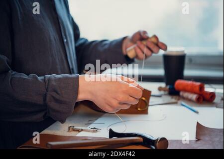 Un jeune cordonnier expérimenté ou tailleur rase un morceau de cuir unique dans un studio lumineux spacieux. Banque D'Images