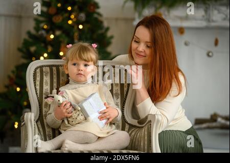 Petite fille blonde dans une chaise et sa mère ensemble Devant l'arbre de Noël Banque D'Images