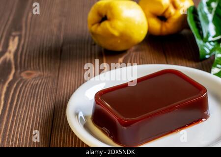 Confiture de coing maison sur la plaque blanche, fruits de coing frais mûrs sur la table en bois. Dessert traditionnel espagnol typique. Banque D'Images