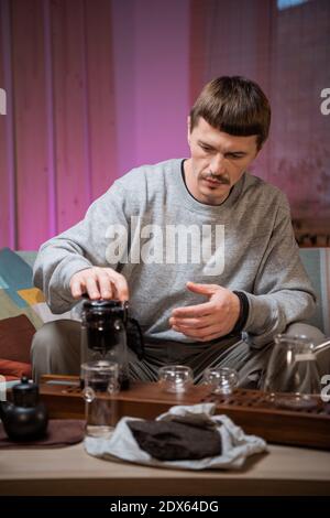 A true master of traditional chinese ceremonies brews aged raw black tea by pouring hot water into the teapot. Tea party in the comfort of home Stock Photo