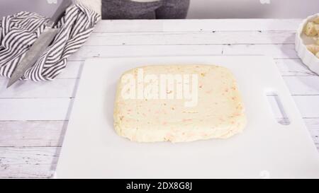 Étape par étape. Coupe de fudge de canne à sucre fait maison sur un tableau de découpe blanc. Banque D'Images