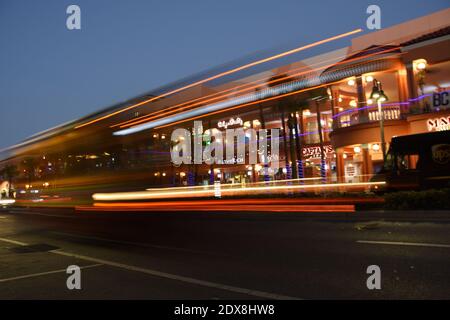 Des pistes lumineuses de l'autobus local sont en mouvement pendant que vous passez devant le centre commercial Strip Mall pendant l'heure bleue à Clearwater, Floride, États-Unis. Technique d'exposition longue. Banque D'Images