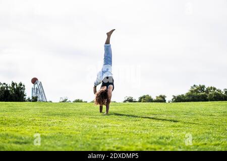 Jeune femme pratiquant la roue à cardans sur l'herbe contre le ciel clair Banque D'Images