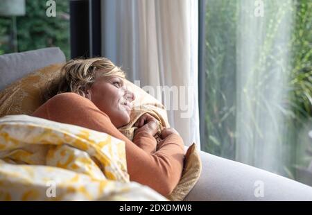 Femme mûre regardant par la fenêtre tout en étant allongé sur le canapé à accueil Banque D'Images