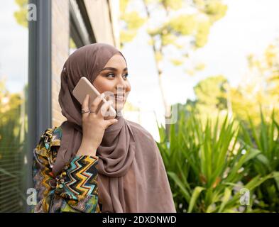 Jeune femme portant le hijab parlant sur un téléphone portable en étant debout à l'extérieur Banque D'Images