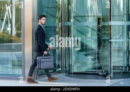 Jeune homme d'affaires portant une mallette en se dirigeant vers un immeuble de bureaux Banque D'Images
