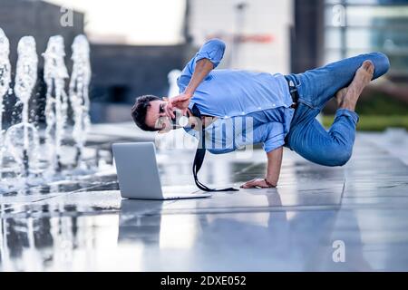 Un jeune homme d'affaires avec un ordinateur portable qui boit du café tout en se faisant tenir à la main fontaine sur le sentier Banque D'Images