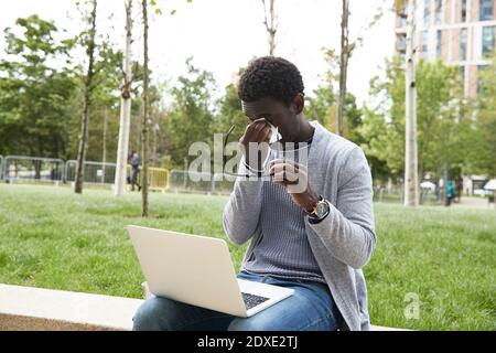 Homme d'affaires essuyant les yeux avec du papier de soie tout en restant assis sur la retenue mur Banque D'Images