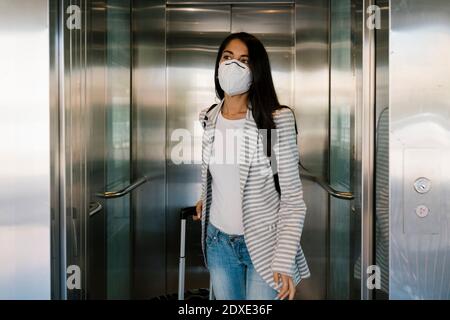 Femme portant un masque facial de protection sortant avec les bagages de ascenseur à la gare Banque D'Images