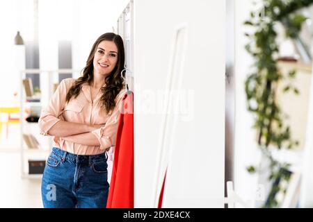 Styliste féminine souriante, bras croisés, penchée sur le support en studio Banque D'Images