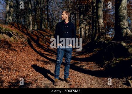 Homme regardant loin en se tenant les mains dans les poches chemin forestier Banque D'Images