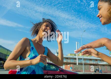 Une jeune femme rit en regardant une amie en ville par beau temps Banque D'Images