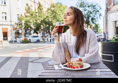 Une jeune femme qui regarde dehors tout en prenant le petit déjeuner en ville Banque D'Images