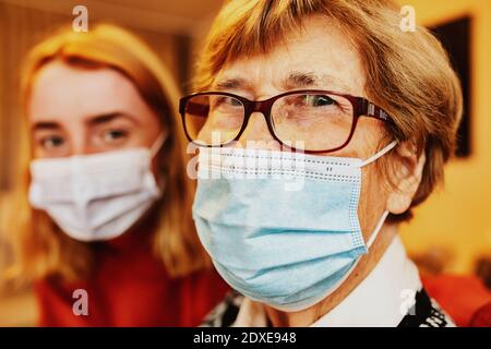 Grand-mère portant un masque facial et des lunettes de vue tout en étant assise petite-fille à la maison Banque D'Images